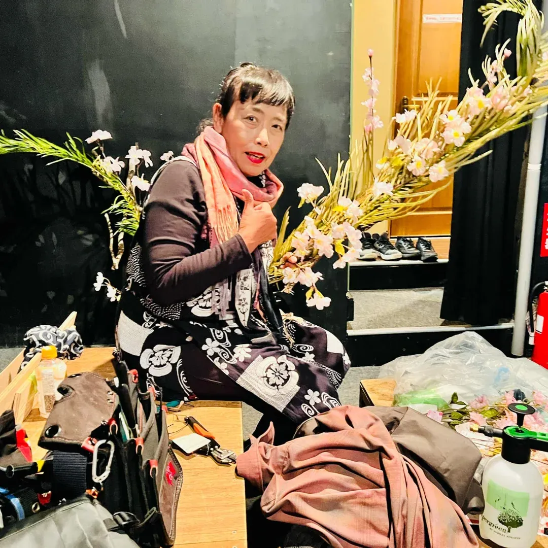 舞台の裏で桜の枝を手に微笑む横井紅炎