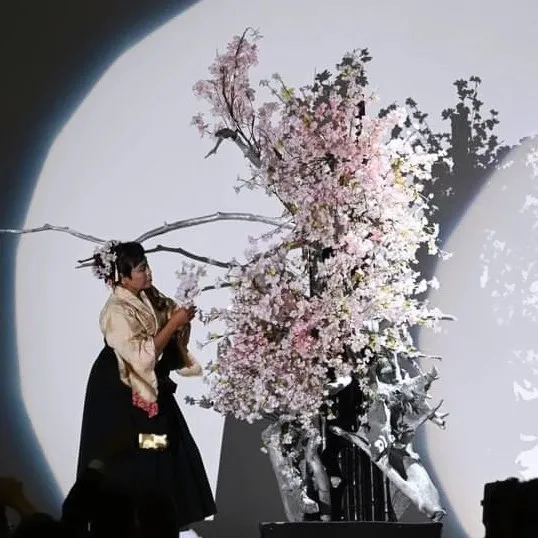 暗い舞台の上、月のような照明を背に桜の大枝をいける横井紅炎